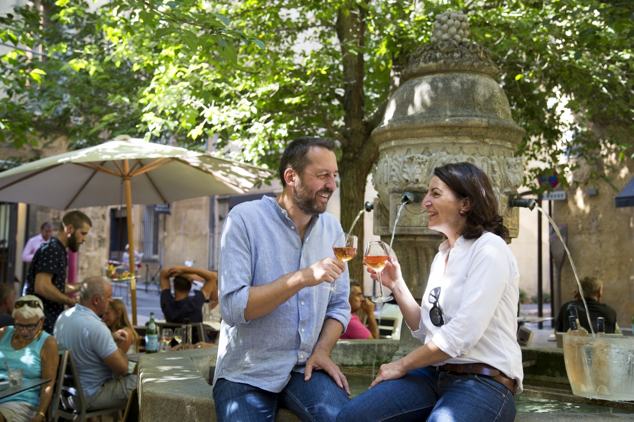 Ein Paar sitzt am Brunnenrand und stösst mit einem Glas Roséwein an